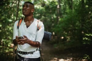 A hiker looks frustrated while using a smartphone to navigate in a dense forest.